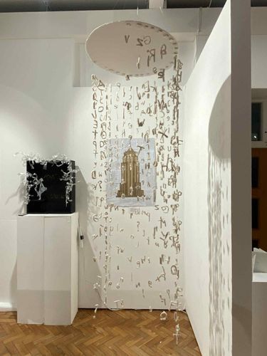 Sculpture made from strings of white letters suspended from disc, hanging in gallery