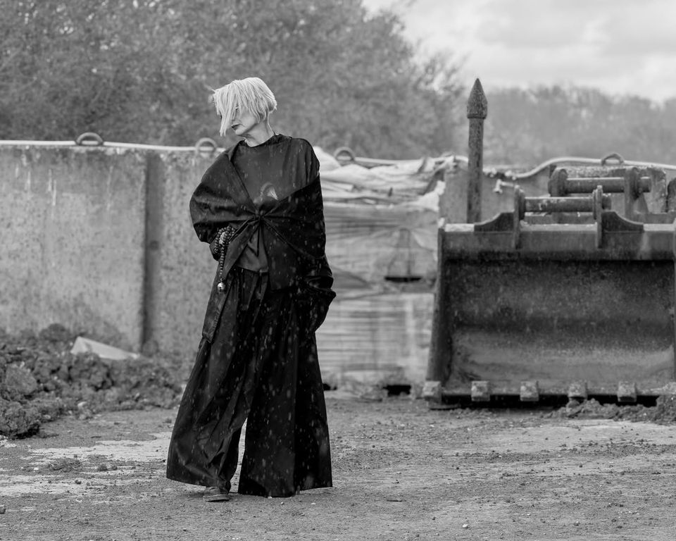 Black and white photo of female model wearing black trouser suit near industrial machinery