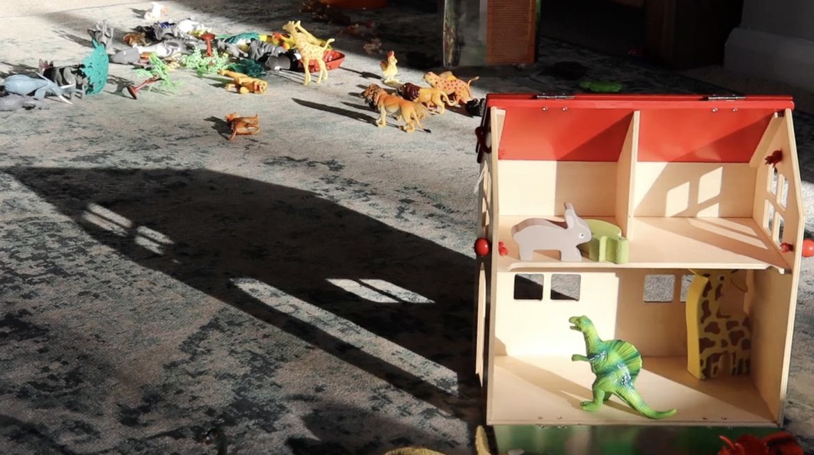 Film still showing a doll's house and various toy dinosaurs and animals