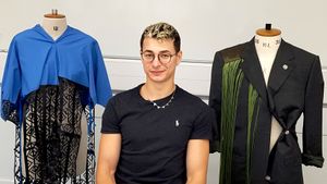 Cosmin Diaconu sitting between two mannequins displaying a blue garment with lace and a black coat with green accents.