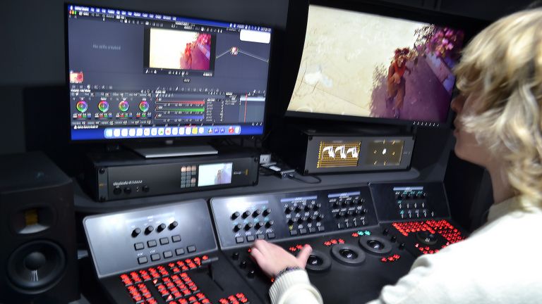 Jacob using a video editing workstation with multiple screens and control panels, adjusting color grading on footage displayed.