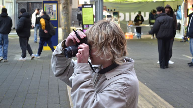 Jacob taking a photo on a street, with people and market stalls in the background.