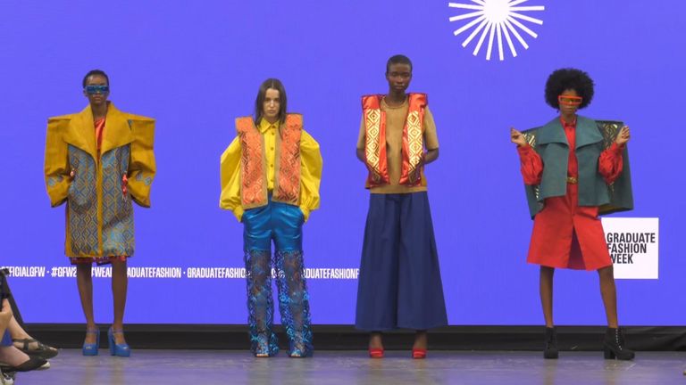 Four models on a runway wearing bold, colorful outfits with intricate patterns and textures against a bright blue background.