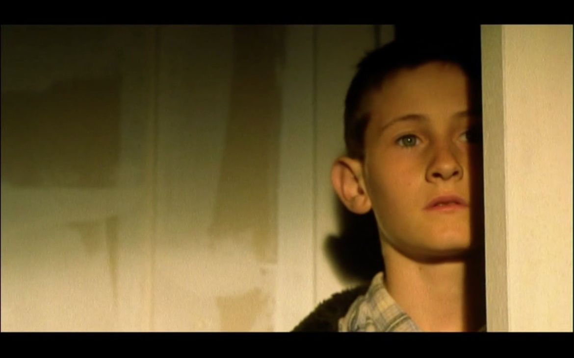 Film still of young boy looking around door