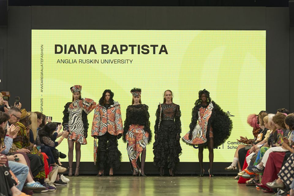 Five models in bold, patterned outfits walk a runway, with a yellow screen displaying "Diana Baptista, Anglia Ruskin University" in the background.