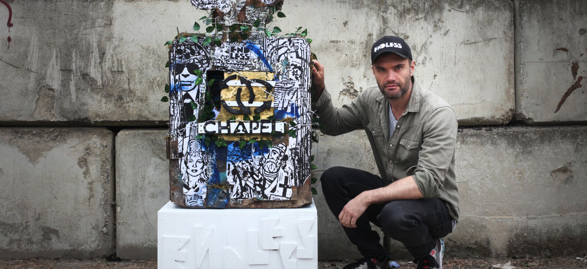 Photo of Endless crouching beside his Chapel perfume bottle sculpture