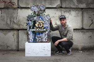 Photo of Endless crouching beside his Chapel perfume bottle sculpture