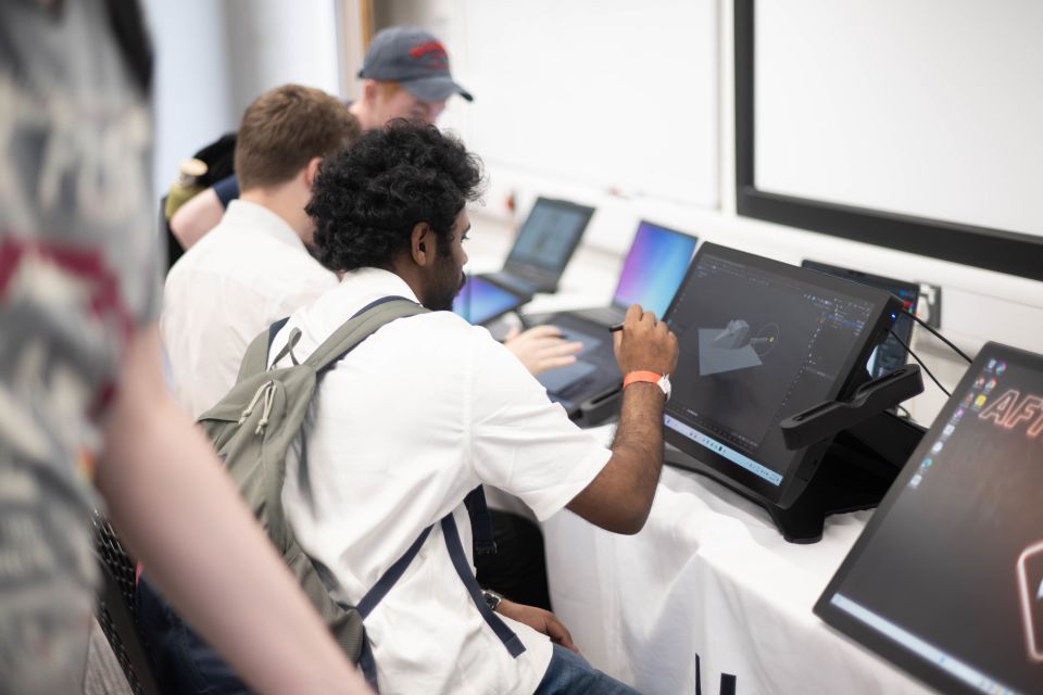 Young men working on digital art at a table with laptops and drawing tablets.
