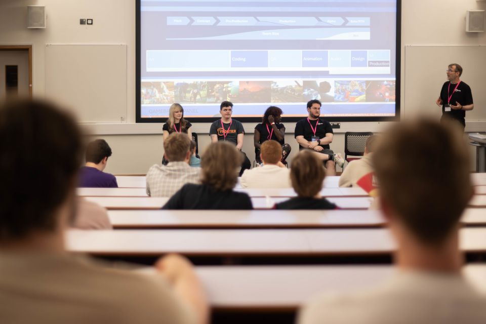 A panel of five people in front of an audience, with images on a giant screen behind them.
