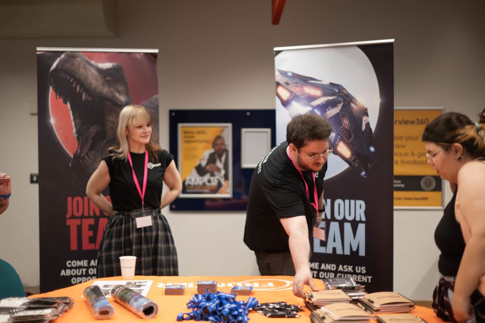Two Frontier reps at a recruitment booth with banners featuring a dinosaur and a spaceship, with promotional materials on the table.in front of them
