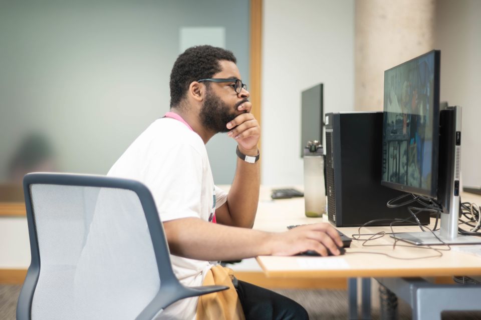 A man in a white shirt and glasses working at a computer, focusing intently on the screen