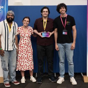 Four people stand smiling in front of Gamebridge festival banners; one holds an award plaque.