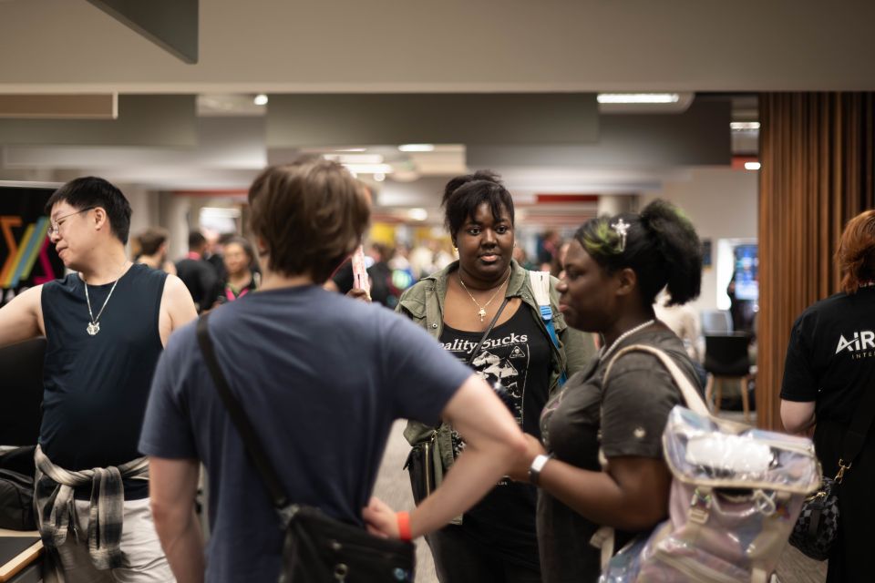 A group of people engaging in conversation at a busy indoor event, with colorful banners in the background.