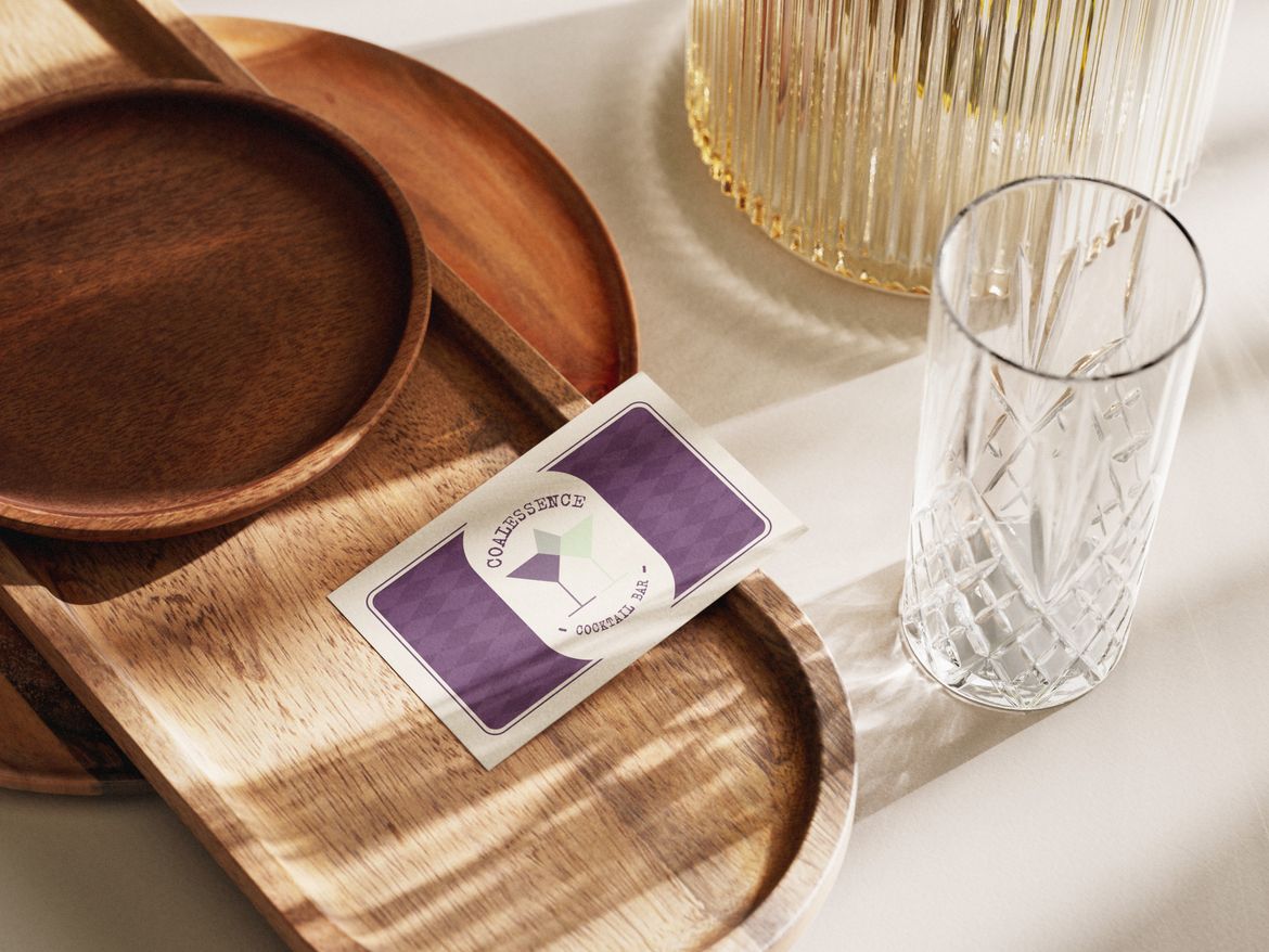Photo of a purple business card with cocktails on, on a wooden tray next to a glass