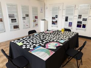 Photo of a table covered in white cards and other leaflets in room with walls covered with posters with text and images