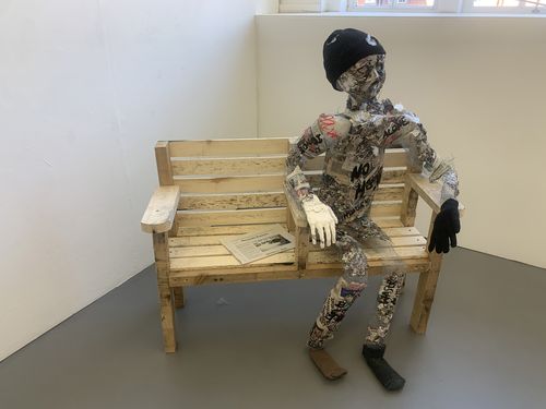 A fake skeleton covered in paper sitting on a bench