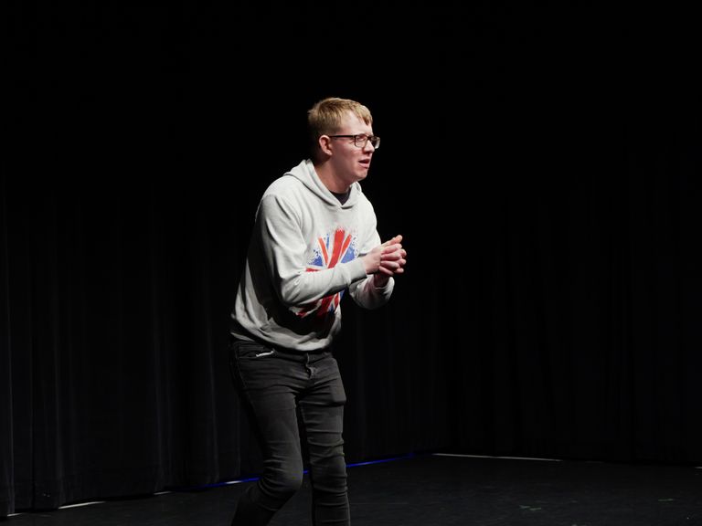 Jack Palmer on stage in Union Jack hoodie, clasping hands together