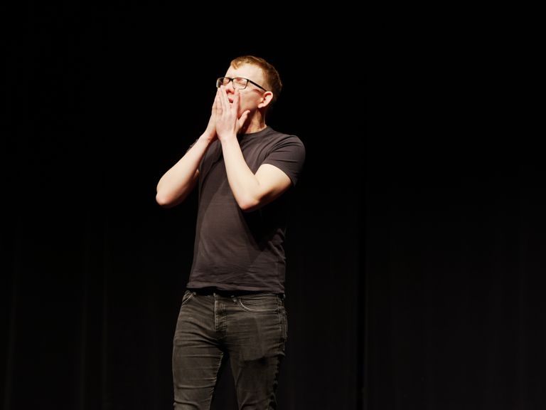 Jack Palmer on stage in front of black curtain, holding face with both hands
