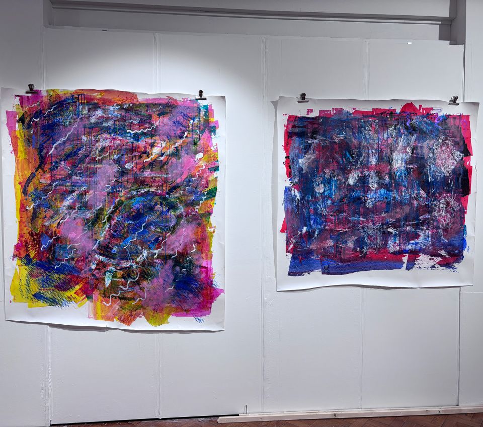 Two abstract paintings with vibrant colors on display, featuring layered brush strokes and dynamic textures.