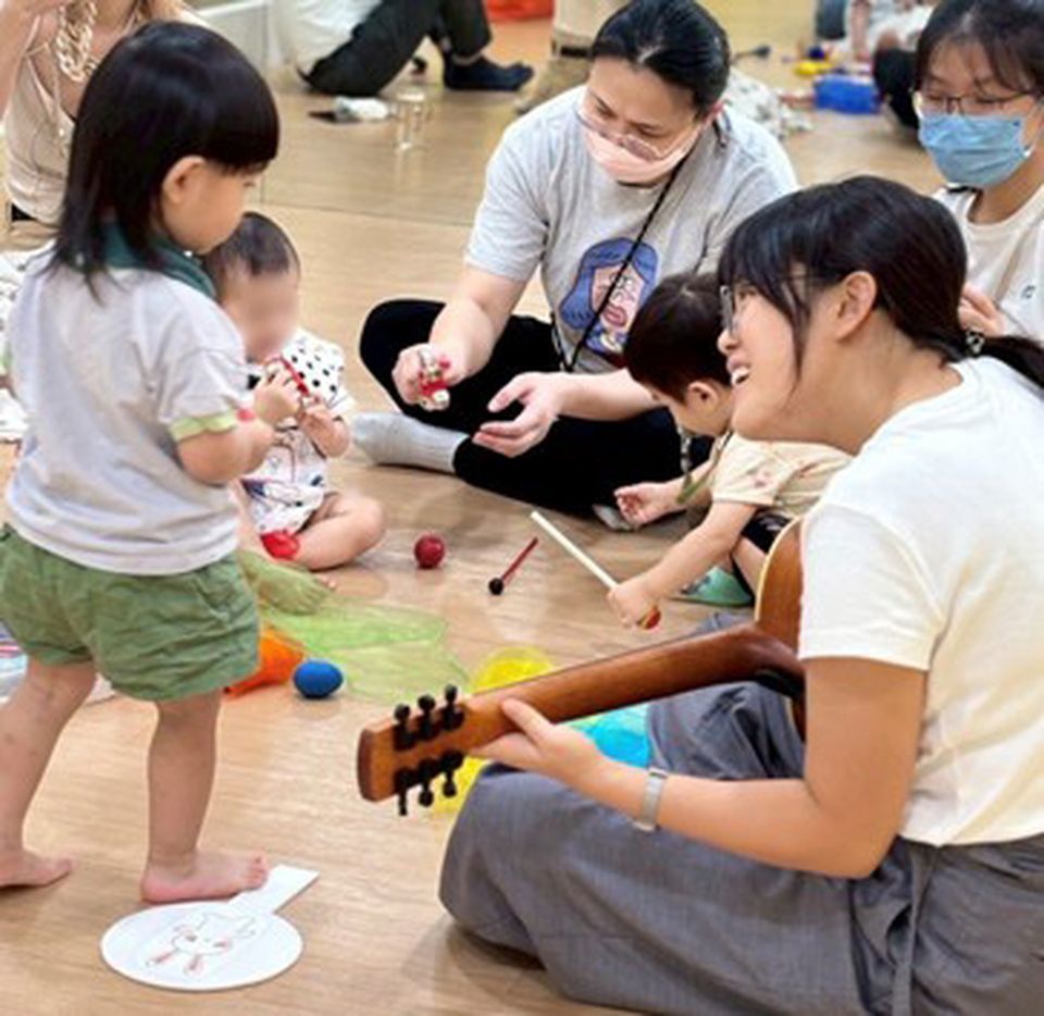 Children and adults engaging in a playful music session; Amanda, holding a guitar, interacts with a child.