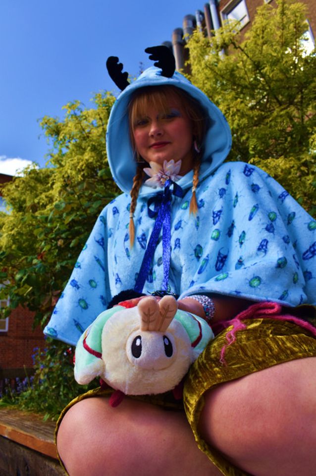 Photo of female model sitting outside wearing blue hoodie with antlers and holding plushie moth