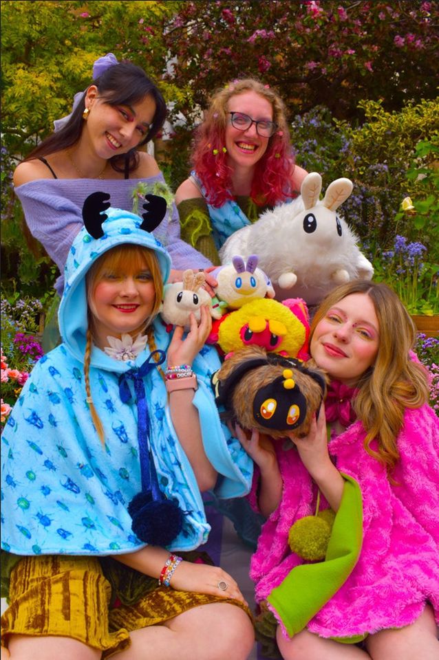 Photo of four female models wearing different bright coloured outfits surrounded by plushie animals