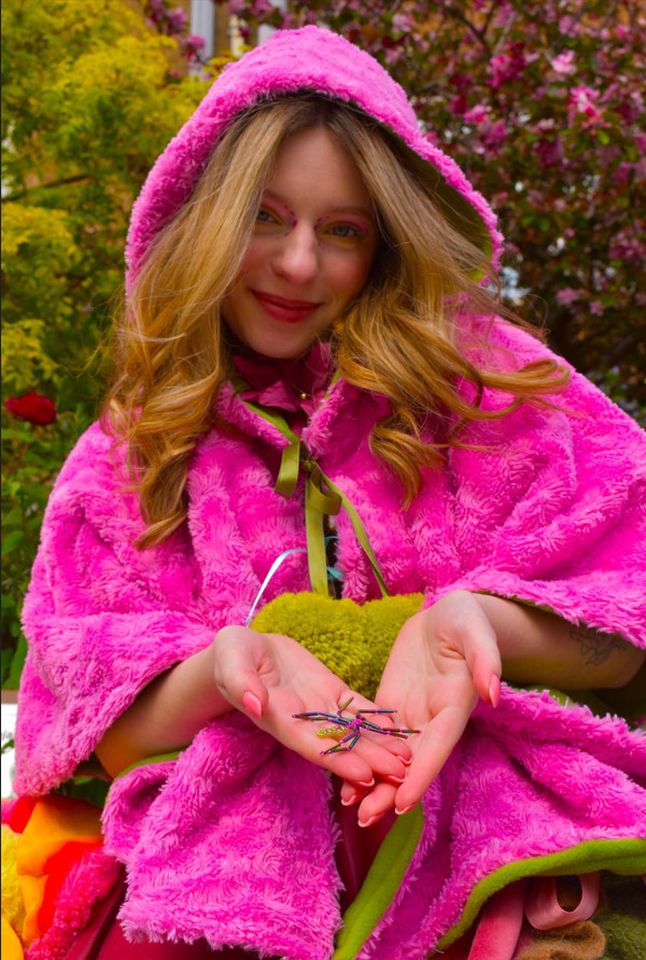Photo of female model wearing pink hoodie and holding plastic spider