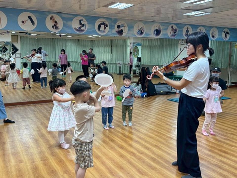 Amanda plays the violin in a dance studio while young children holding paper plates watch and listen attentively.