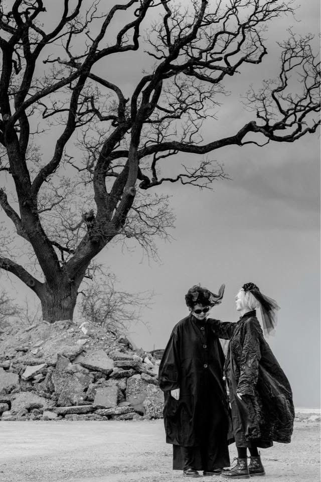 Black and white photo of two female models wearing sunglasses and black outfits near bare tree