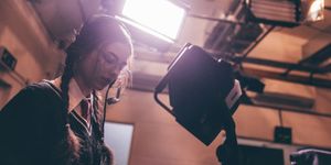 Female student in film studio using camera and talking into headset