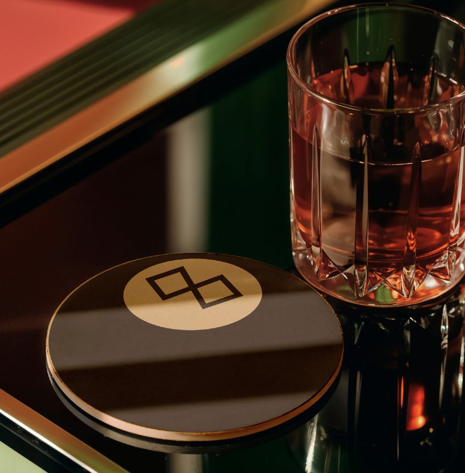 Photo of a coaster shaped like a no. 8 pool ball next to a glass of drink