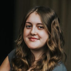 Young woman with wavy, shoulder-length hair, smiling softly against a dark background.