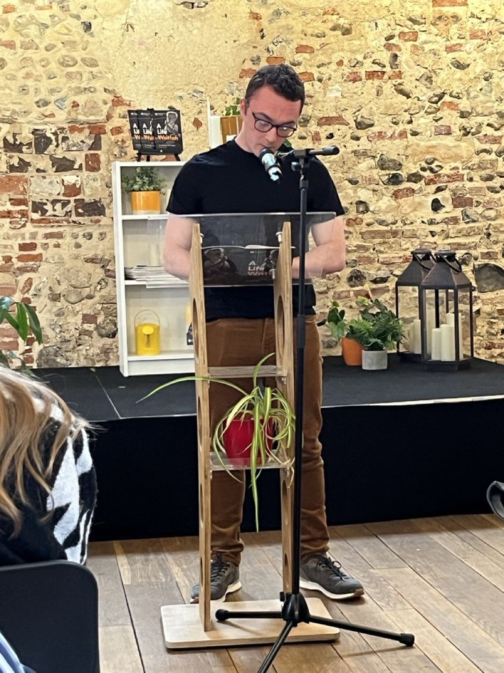 Will Hardy standing at a wooden lectern and speaking into microphone