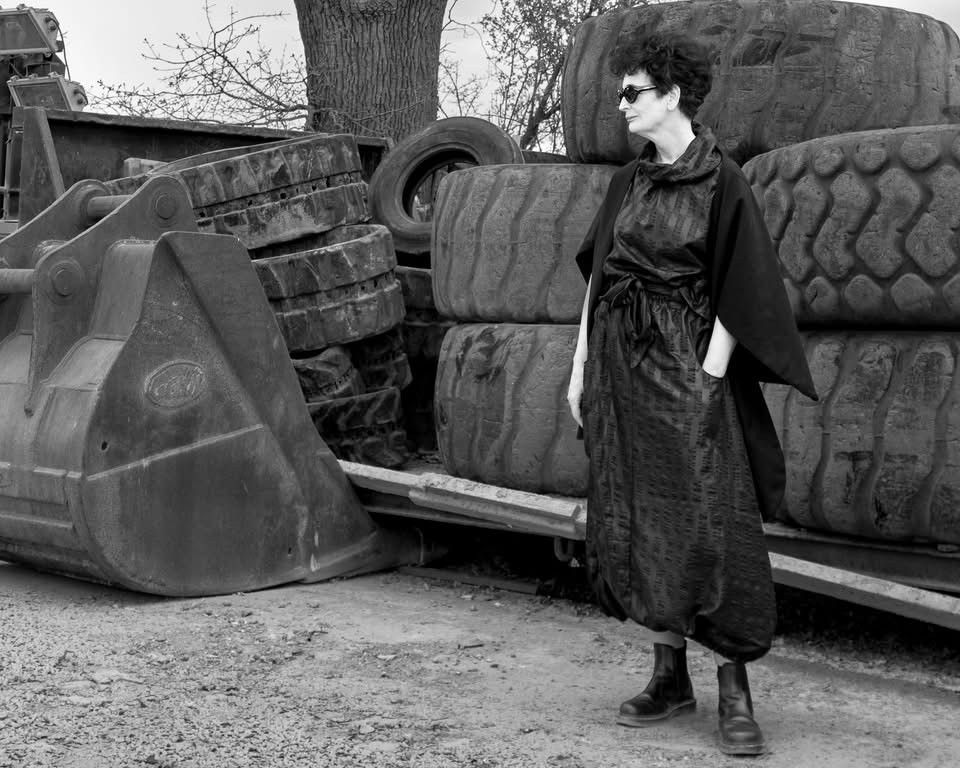 Black and white photo of female model wearing black sunglasses and dress near industrial machinery