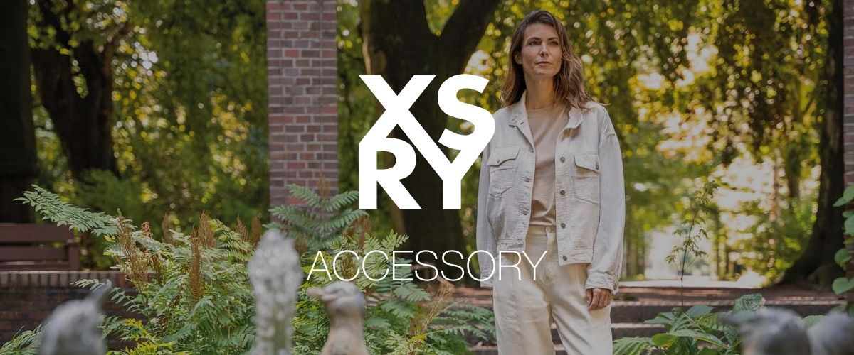 Eine Frau in heller Kleidung steht in einer Gartenkulisse. Das Logo der Marke XSRY überlagert das Bild.