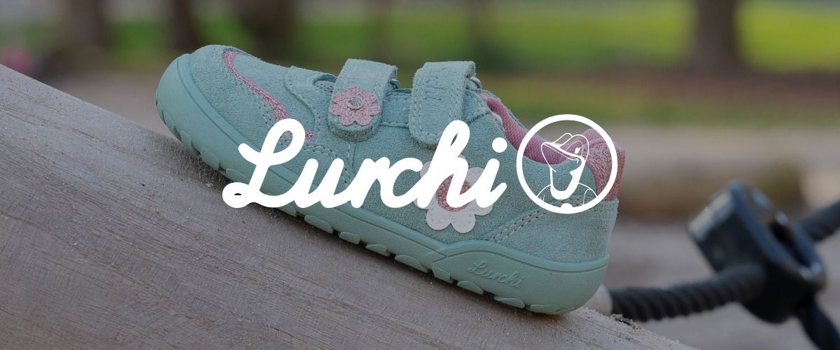 Mintgrüner Kleinkindschuh mit rosa Akzenten und Blumenmuster auf einem umgestürzten Baumstamm. Das Logo der Marke Lurchi überlagert das Bild.
