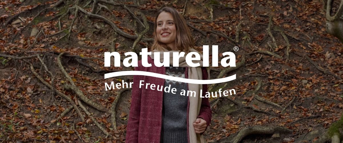 Eine Frau steht in einer Waldlandschaft mit freiliegenden Baumwurzeln und abgefallenem Laub. Das Logo der Marke naturella überlagert das Bild.