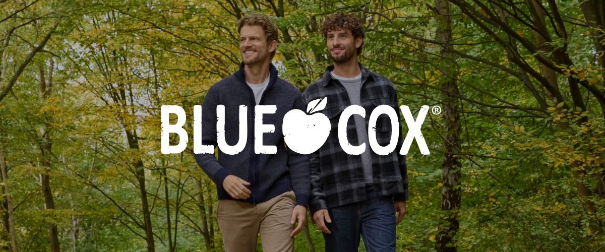 Zwei Männer, die auf einem Waldweg spazieren gehen, umgeben von grünen Bäumen. Das Logo der Marke BLUE COX überlagert das Bild.