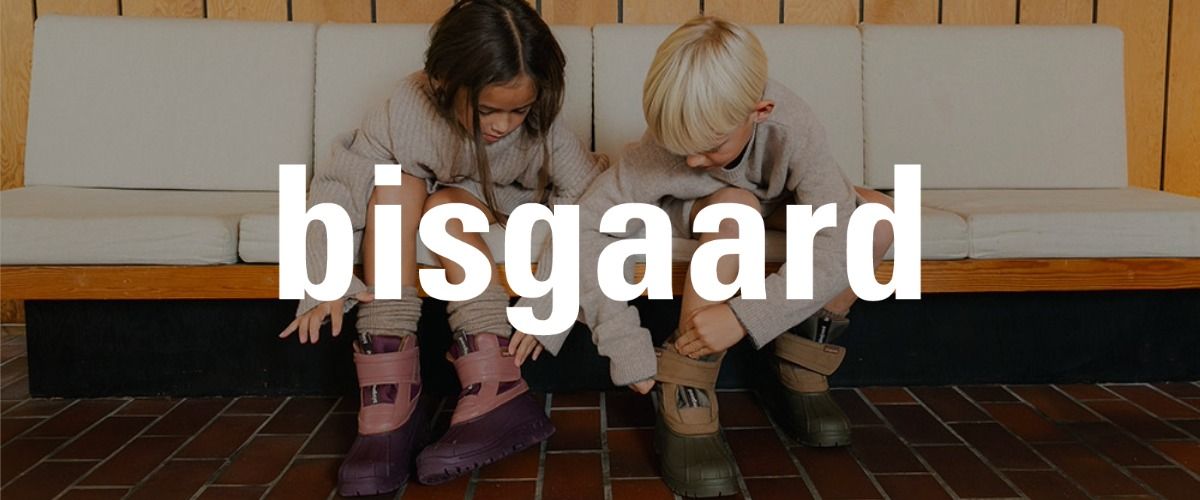 Zwei Kinder sitzen auf einer Bank und ziehen ihre Stiefel an. Das Logo der Marke bisgaard überlagert das Bild.