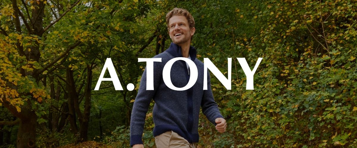 Ein Mann, der einen marineblauen Pullover trägt, geht spazieren. Im Hintergrund sind grüne Bäume zu sehen. Das Logo der Marke A. TONY überlagert das Bild.