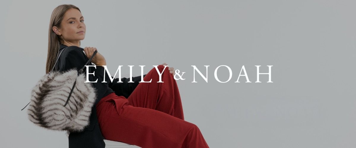 Vor einem grauen Hintergrund sitzt eine Frau mit einer gestreiften Pelztasche und einer roten Hose auf einem Stuhl. Das Logo der Marke EMILY & NOAH überlagert das Bild.