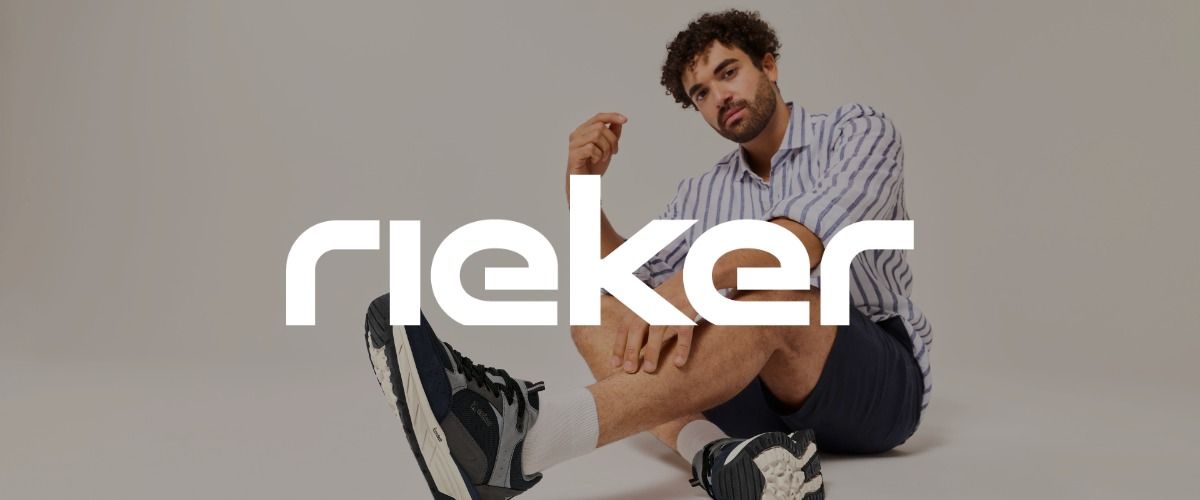 Ein Mann in gestreiftem Hemd und Shorts sitzt mit gekreuzten Beinen auf dem Boden und trägt Turnschuhe. Das Logo der Marke Rieker überlagert das Bild.