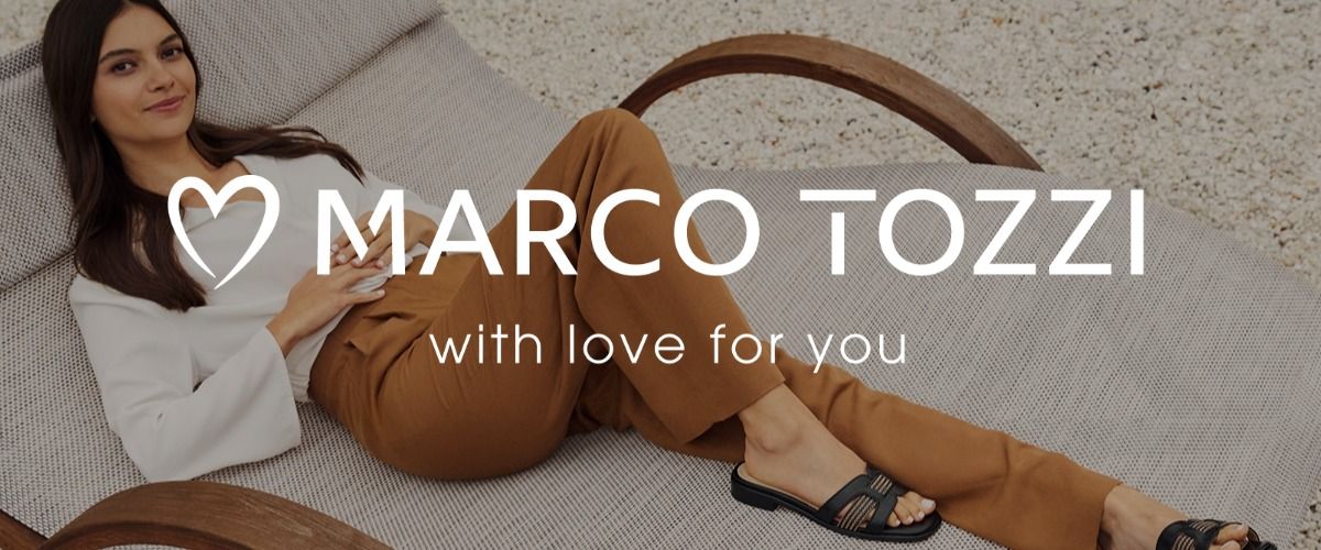 Frau, die sich auf einem Liegestuhl entspannt, trägt eine braune Hose und schwarze Sandalen. Im Vordergrund ist das Logo der Marke Marco Tozzi mit dem Claim "with love for you" zu sehen.