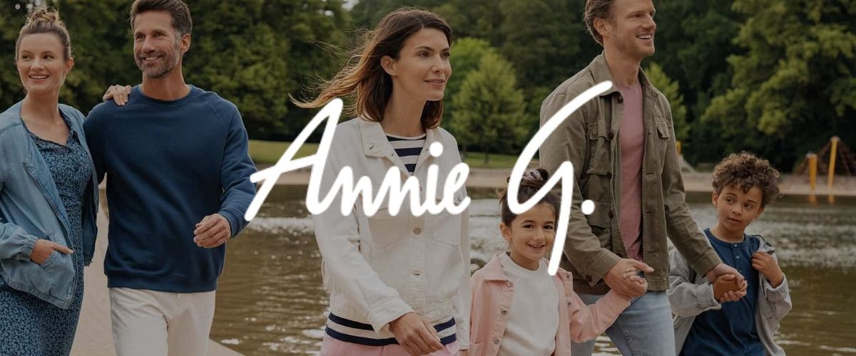 Eine Gruppe von Erwachsenen und Kindern, die fröhlich an einem Teich entlangspazieren. Das Logo der Marke Annie G. überlagert das Bild.
