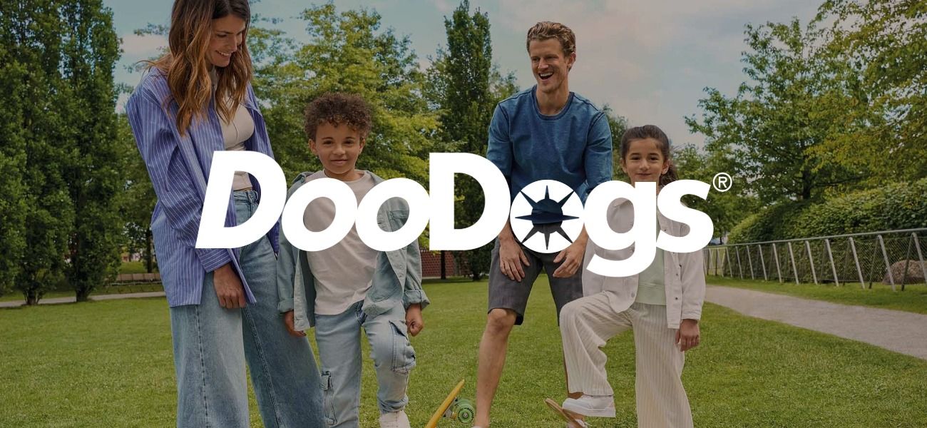Eine Familie steht auf einer Wiese mit Bäumen im Hintergrund. Das Logo der Marke DooDogs überlagert das Bild.