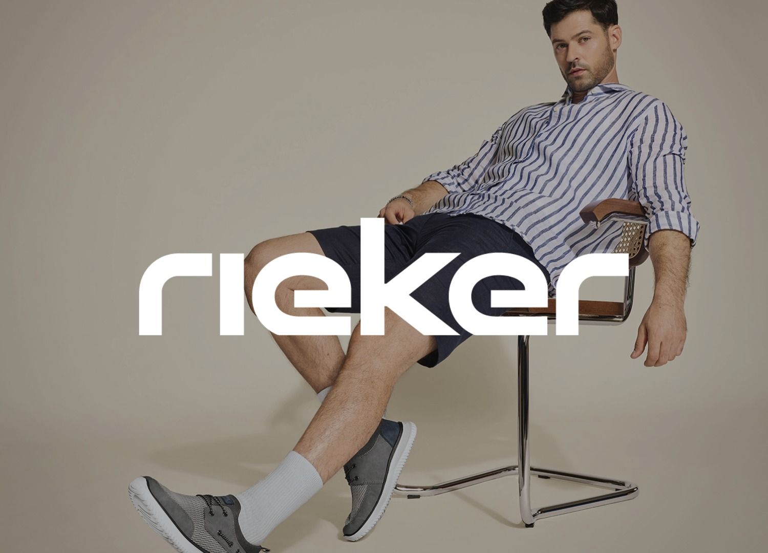 Ein Mann in einem gestreiften Hemd und Shorts sitzt entspannt auf einem Stuhl und trägt graue Schuhe. Das Logo der Marke Rieker überlagert das Bild.