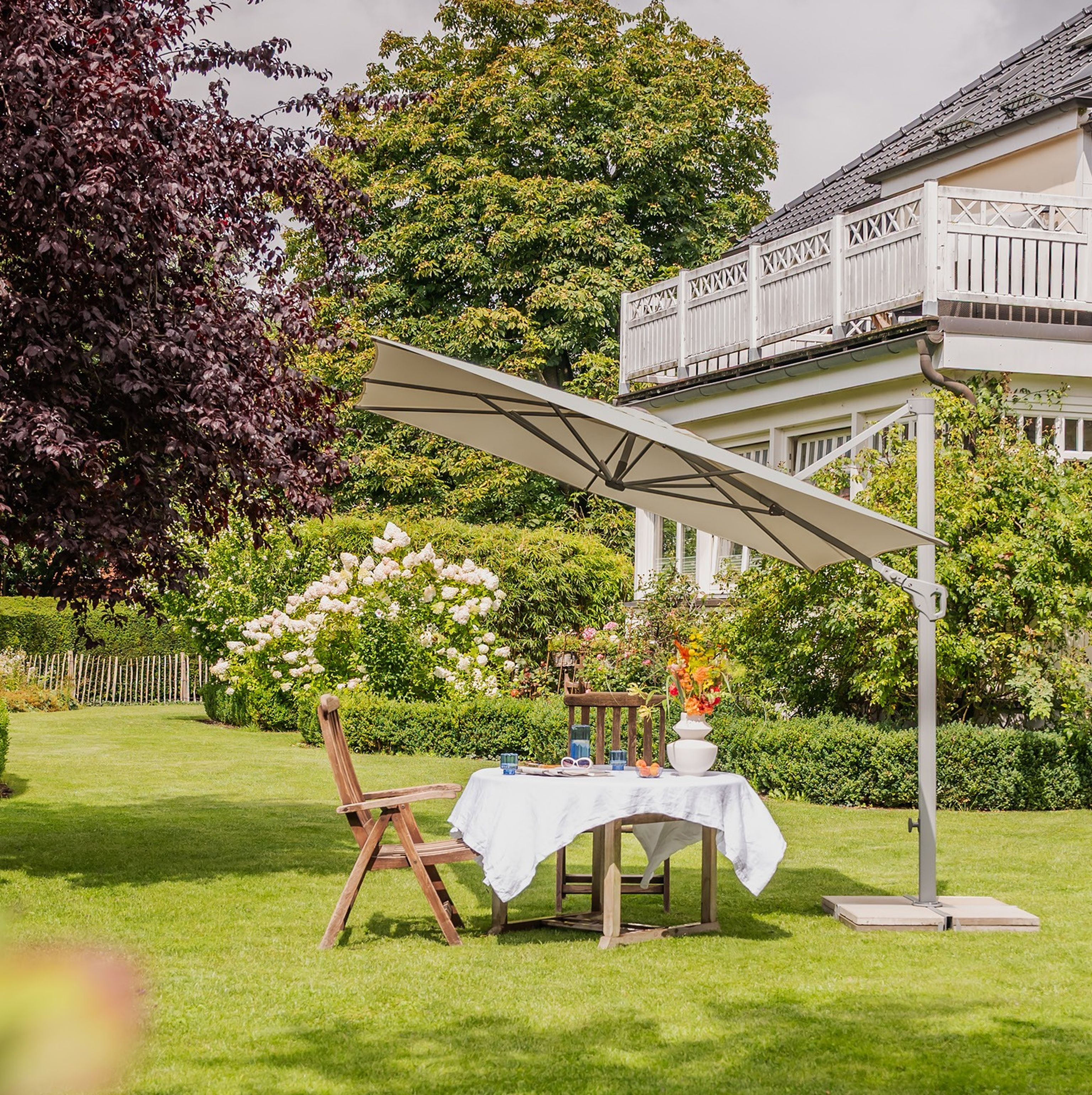 Ein Garten in dem ein Sonnenschirm steht, der einem Tisch Schatten spendet.