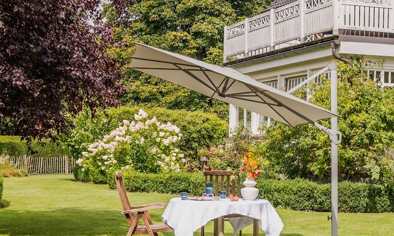 A garden with a parasol providing shade for a table.