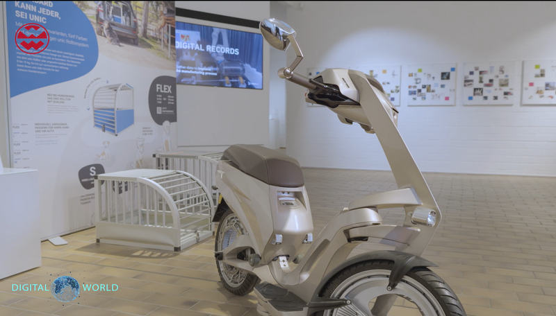 A sleek, modern electric scooter displayed in a showroom with informational posters and framed photos on the wall.
