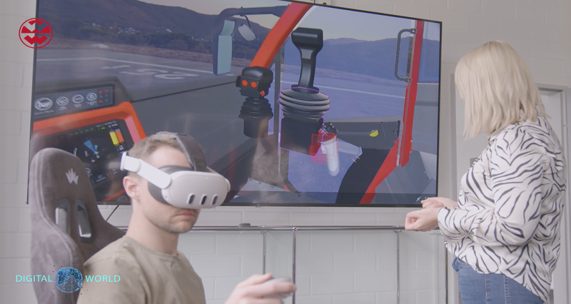 A person wearing a VR headset is seated, controlling a simulation on a large screen. Another person stands nearby, observing the display.
